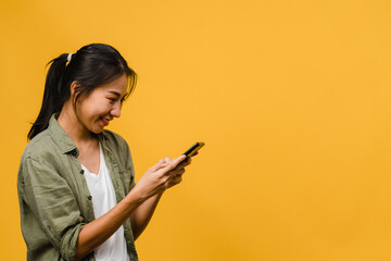 Wall Mural - Young Asia lady using phone with positive expression, smiles broadly, dressed in casual clothing feeling happiness and stand isolated on yellow background. Happy adorable glad woman rejoices success.