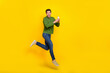 © deagreez - Photo of attractive impressed guy dressed green pullover jumping reading modern gadget empty space isolated yellow color background