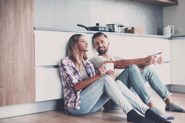 Wall Mural - young couple drinking coffee sitting on the kitchen floor