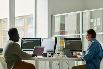 two it specialists sitting at table with computers at office and writing new codes on their laptop t