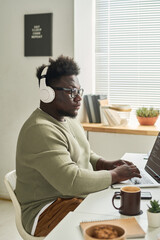african young software developer in wireless headphones concentrating on his online work on laptop