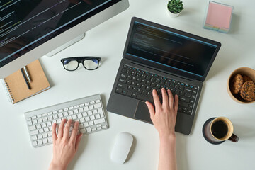 Wall Mural - High angle view of young programmer writing code on laptop and using computer keyboard at table