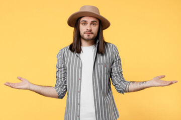 Wall Mural - Young man he 20s wears striped grey shirt white t-shirt hat spread hands shrugging shoulders looking puzzled, have no idea isolated on plain yellow color background studio. People lifestyle concept.