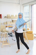 © feeling lucky - Active young beautiful asian housewife woman cleaning with vacuum cleaning floor after working SME with E-commerce Package box background. Cleaning girl in muslim black leggings vacuuming her room.