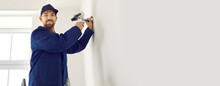 Professional Young Male Technician Installs Surveillance Camera Inside Office Or Apartment. Portrait Of Friendly Worker In Workwear Who Attaches Cctv Camera To White Blank Wall. Copy Space. Banner.