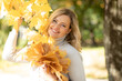Autumn portrait of charming blonde inlight cashmere sweater with bouquet of leaves in her hands, walking in park.