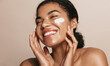 Leinwandbild Motiv Smiling woman using skincare product. Female taking face cream to apply on facial skin