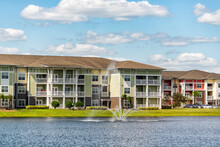 Orlando, Florida Luxury Lifestyle Apartments Buildings With Three Floors By Lake Water Fountain In Tropical City With Blue Sky Clouds