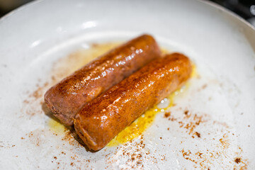 Closeup of two vegan meat replacement fake sausages cooking on ceramic nonstick frying pan in oil with crispy skin