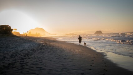 Wall Mural - Silhouettes of a person running with their dog on the sandy beach against ocean waves at sunset