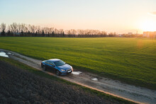 Aerial View Of Sedan Car Driving Fast On Dirt Road At Sunset. Traveling By Vehicle Concept