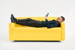 © GVS - Relaxed man lying on yellow sofa using smartphone