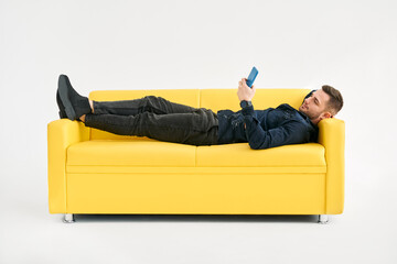 Relaxed man lying on yellow sofa using smartphone