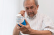 Asian senior man with farsighted reading prescription on medicine bottle at nursing home. Medical insurance and health care concept