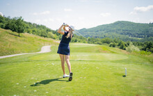 Pretty Sportswoman Hitting The Ball With Golf Club. Professional Female Golfer Holding Golf Club On Field And Looking Away. Young Woman Standing On Golf Course On A Sunny Day.
