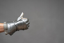 Male Hand In Plate Armor Mitten Shows A Thumbs Up Gesture On The Gray Background Close Up.
