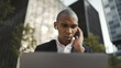 © Drobot Dean - Adult african american businessman using laptop and earphones outdoors