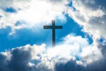Wall Mural - Silhouette of Christian cross over clouds against sky in the background. Easter religion faith concept