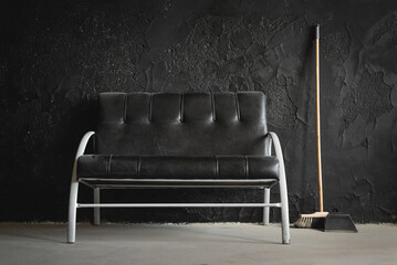 Wall Mural - Black dirty sofa, broom and dustpan on the black wall background.
