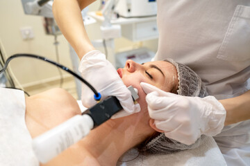 Wall Mural - Beautician applying rejuvenation treatment on young woman face in beauty salon