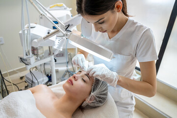Wall Mural - Beautician squeezing and removing manually blackheads from female client's face during the cosmetic procedure in beauty salon.