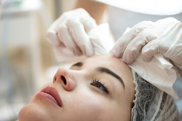 Wall Mural - Cosmetologist squeezes acne on female patients forehead with wipes in beauty salon