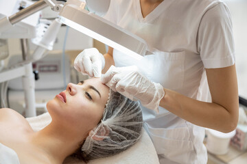 Wall Mural - Cosmetologist squeezing acne on female patients forehead with wipes in beauty salon