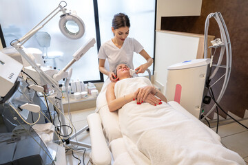 Wall Mural - Young woman getting face skin care rejuvenation with rf lifting electric apparatus in professional beauty salon.
