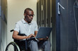 © Seventyfour - Portrait of African American man with disability using laptop in server room while working as IT technician