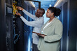 © Seventyfour - Waist up portrait of two system managers inspecting server cabinets in data center, copy space