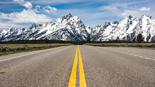 A Road Stretches To The Horizon. Mountains Reach To The Sky In The Distance. Grand Teton National Park, Wyoming.