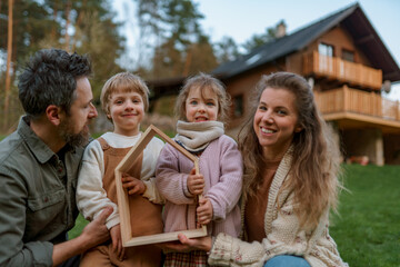 Wall Mural - Happy family is standing near their modern house, smiling and looking at camera