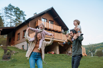 Wall Mural - Happy parents with small children on piggybacks running and having fun together in garden near their house.