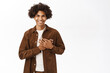 © Cookie Studio - Portrait of smiling gay man holding hands on heart. Queer guy smiling with care, express sympathy, stands over white background