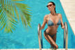 © New Africa - View of beautiful green tropical leaves and woman in bikini getting out of swimming pool
