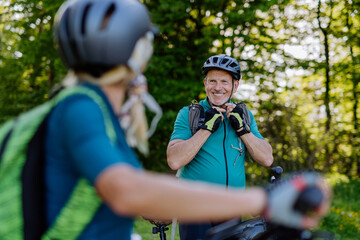 Wall Mural - Active senior couple riding bicycles at summer park, man is putting on helmet, healthy lifestyle concept.