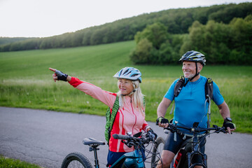 Wall Mural - Active senior couple riding electric bicycles on road at summer park, healthy lifestyle concept.