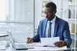 © Seventyfour - Portrait of successful black businessman wearing suit marking data report with pen in office, copy space