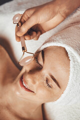 Wall Mural - patient receiving anti-aging face massage with jade roller face massager at spa salon. beauty skin. 