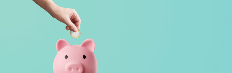 man depositing coins in a pink piggy bank on a blue background - savings concept