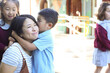 © Austockphoto - Young boy in school uniform hugging his mum while his sister looks on