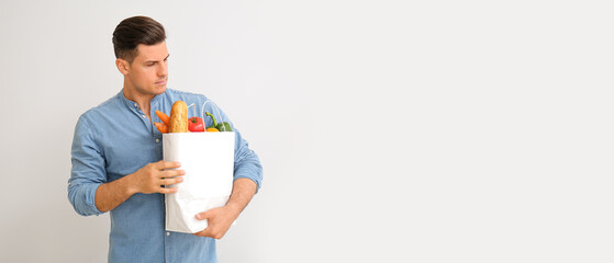 Wall Mural - Young man with paper bag full of food on light background with space for text