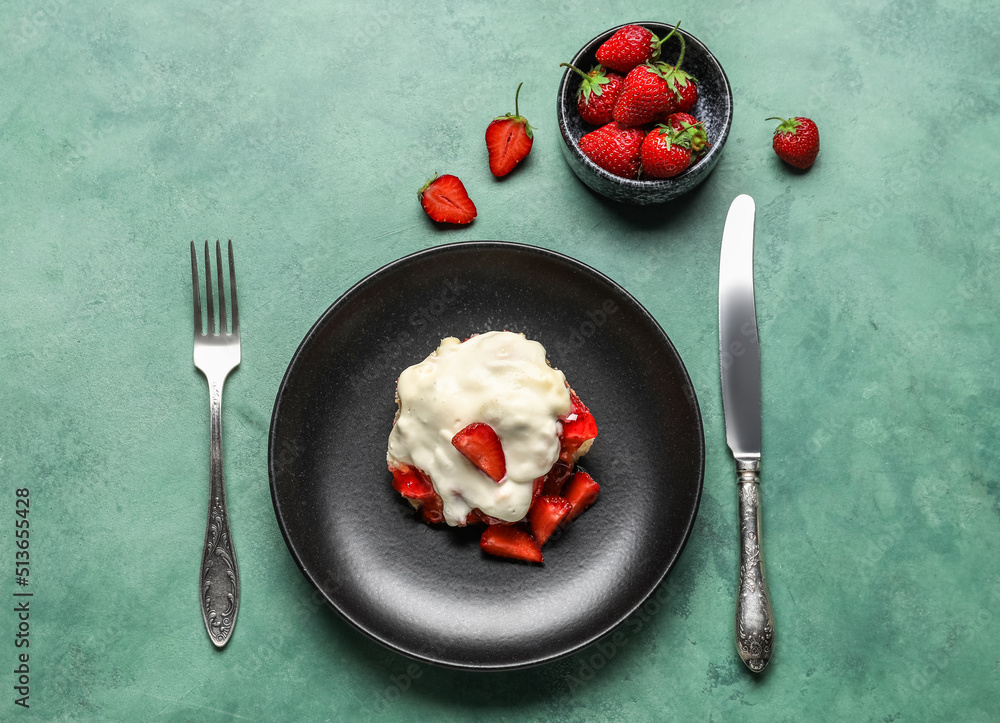 Plate with strawberry cinnamon roll and cutlery on green background