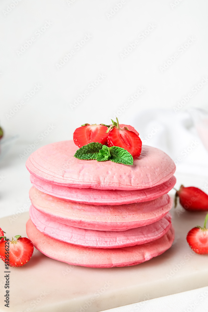 Board with tasty pink pancakes and strawberry on table, closeup
