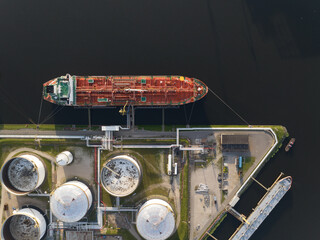 Petrochemical energy heavy transport industry cargo vessel tanker top down aerial drone view. Docked bulk carrier ship along storage facility silos. Energy gas and lpg petroleum commercial industry.