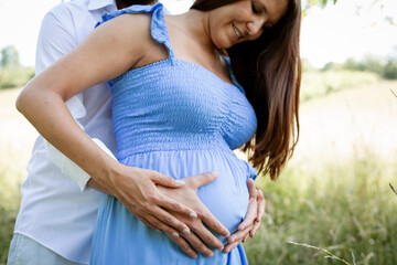 Wall Mural - young couple in love standing in high flower meadow in summer and cuddling and the woman is pregnant and has a blue dress on and the man has a full beard