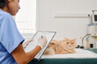 © pressmaster - Hispanic woman working in veterinary clinic standing in front of cat holding clipboard filling in medical form