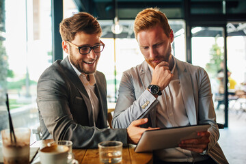 Poster - Happy young business people drinking coffee and working with tablet at cafe.