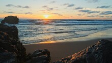 Beautiful Natural Landscape With Sandy Beach  With Big Stones During Sunset.  Sun Over Horizon And Rolling Ocean Waves To The Rocky Shore While Sunset.  Summer Tourist Destination In Portugal. Travel
