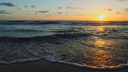 Poster - Beautiful sandy beach while sunset. Beautiful seascape of a sandy beach. Sun over horizon and  rolling ocean waves to the shore while sunset. Summer, travel and tourism. Beautiful wild nature.